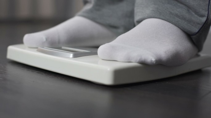 肥胖男子在健康秤上测量体重，节食减肥