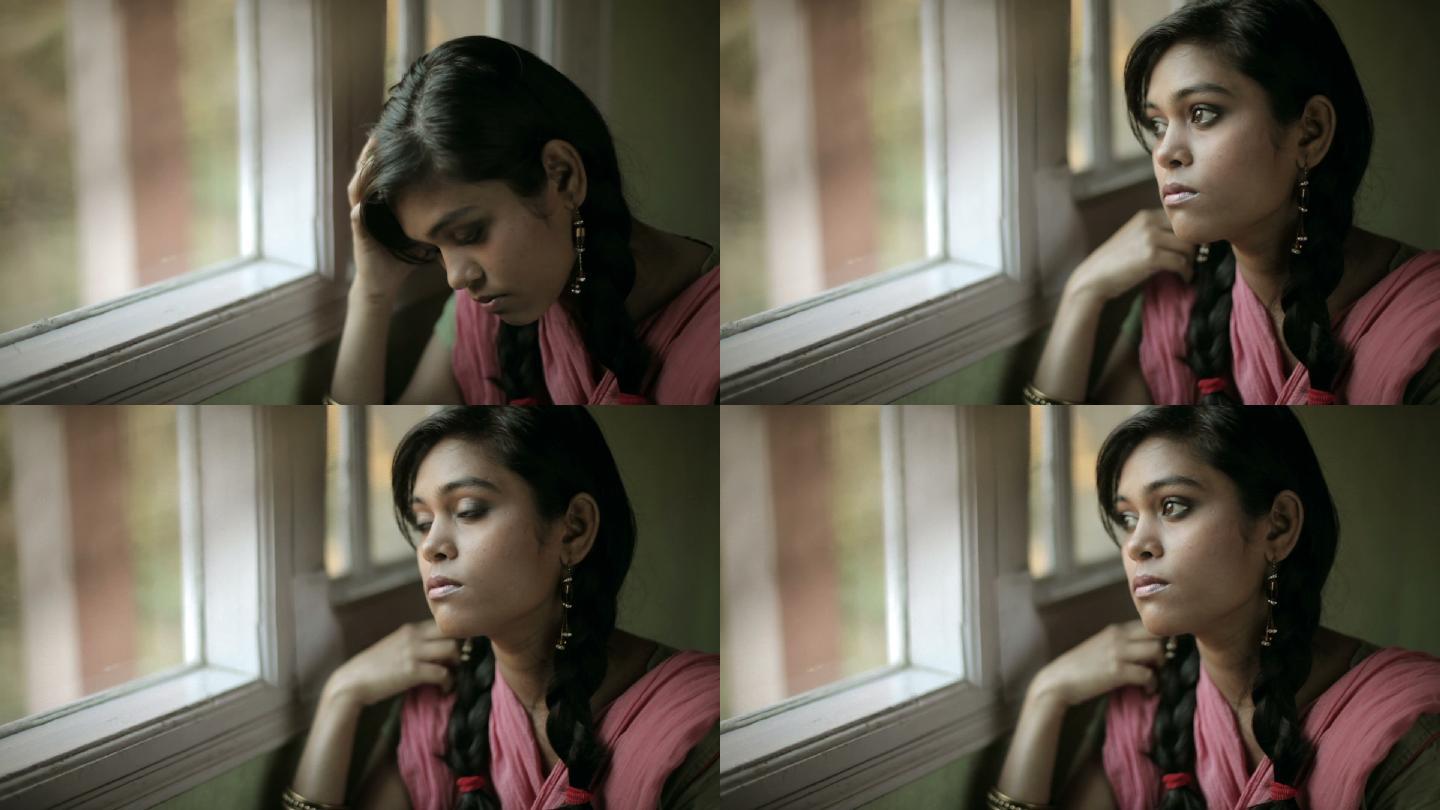 坐在窗边悲伤的少女的室内特写镜头。