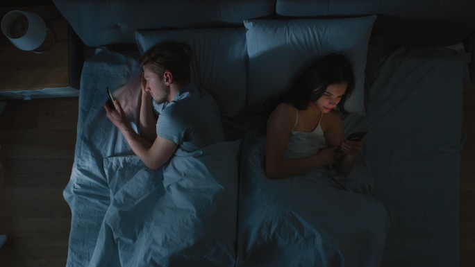 年轻夫妇躺在床上用智能手机