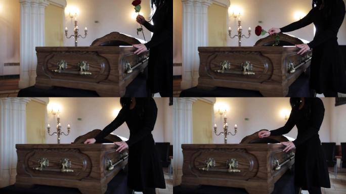悲伤的女人在葬礼上把红玫瑰放进棺材