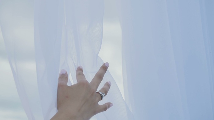 女性的手轻轻地抚摸着白色的窗帘。
