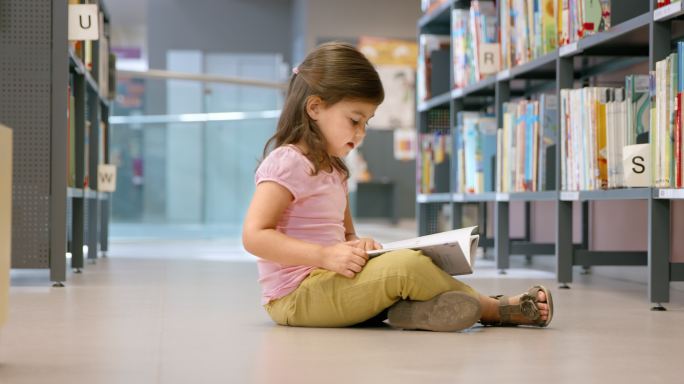 小女孩坐在图书馆的地板上看书