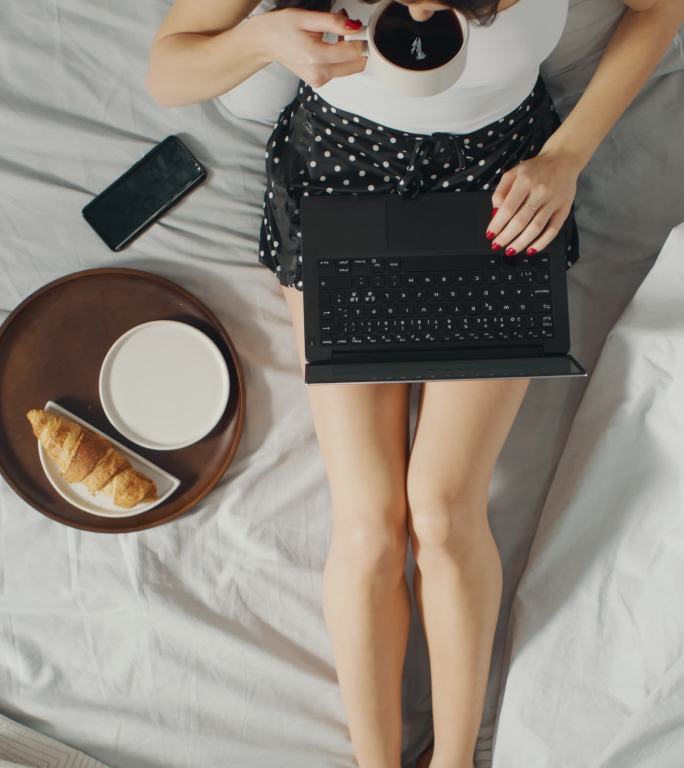 女孩坐在床上用笔记本电脑，并吃面包喝咖啡