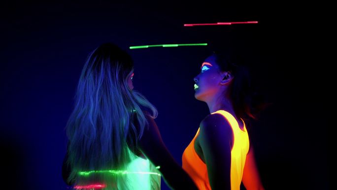 在紫外线黑光下穿着荧光服的两名女子在跳舞