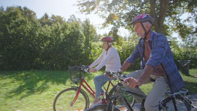 一对老年夫妇骑车穿过阳光明媚的公园