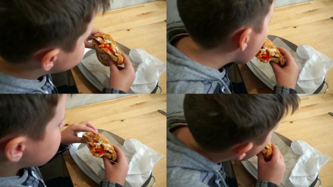 在咖啡馆吃汉堡包的少年。