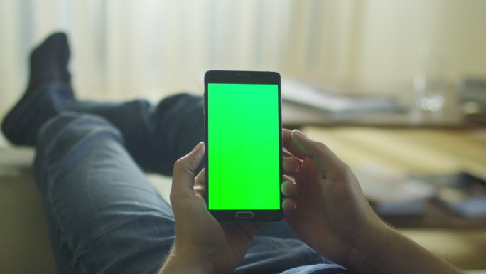 这名男子躺在沙发上使用带有绿色屏幕的手机