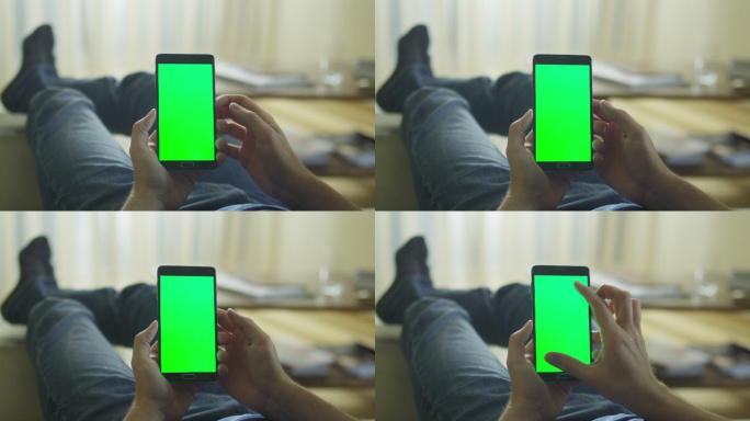 这名男子躺在沙发上使用带有绿色屏幕的手机