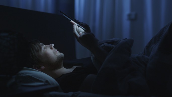 这名男子晚上在家里的床上使用手机