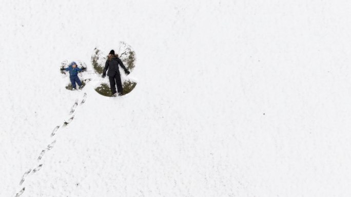母亲和儿子在一个大雪地里做雪天使