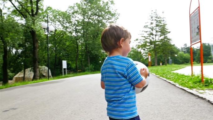 一个手拿球的小男孩在操场上跑步