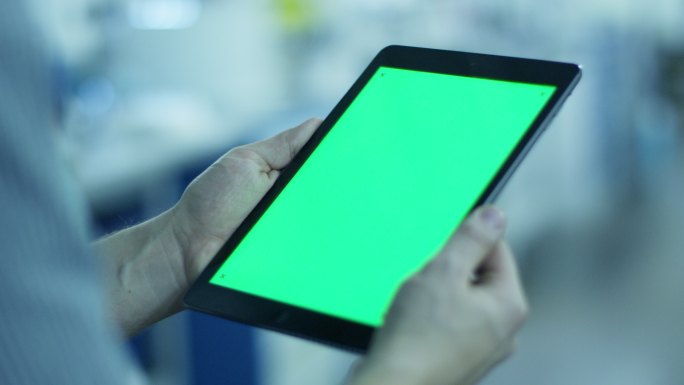 在工厂里，工人拿着绿色屏幕的平板电脑 。