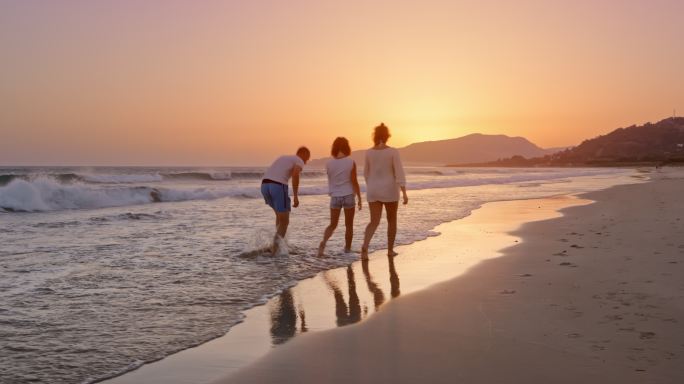 日落时分，一对男女和女儿在沙滩上散步聊天