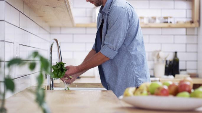 一个年轻人在家里的厨房水槽里洗蔬菜