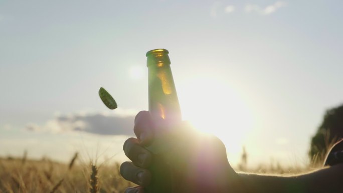 日落时分在麦田附近打开酒瓶的轮廓