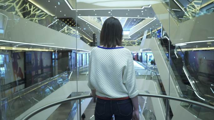 女人爬上购物中心的电梯，从后面看