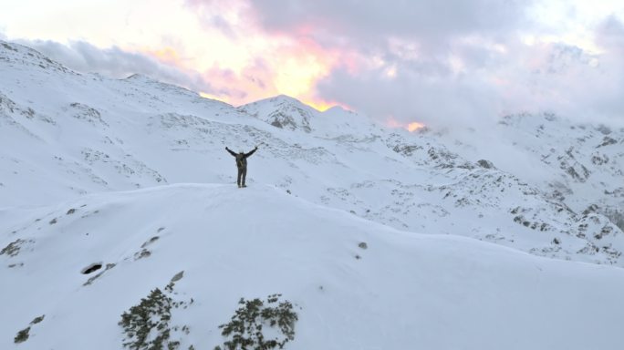 冬季空中登山运动员在山顶上胜利地举起双手
