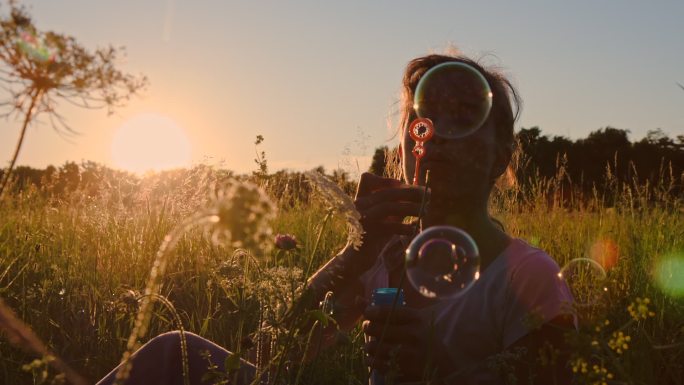 一个女孩日落时在草地上吹泡泡的慢镜头