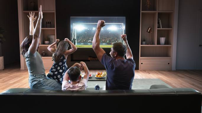 一家人正在电视上观看足球比赛并庆祝进球