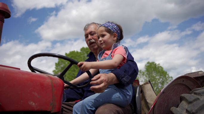 可爱的女孩坐在拖拉机上探索家庭牧场