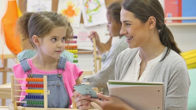 开朗的女幼儿教师帮助学生学习数学卡片