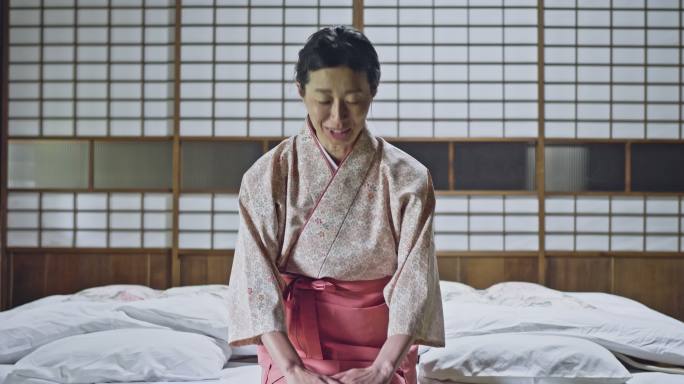 日本女人跪在垫子上，对着镜头打招呼