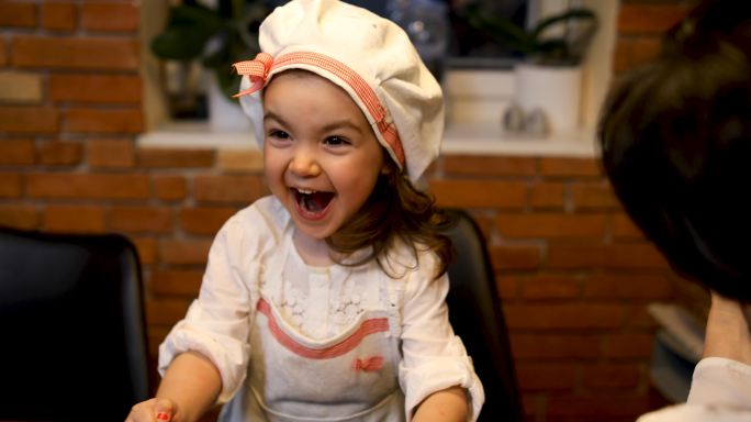 快乐的小女婴在厨房的餐桌旁做菜