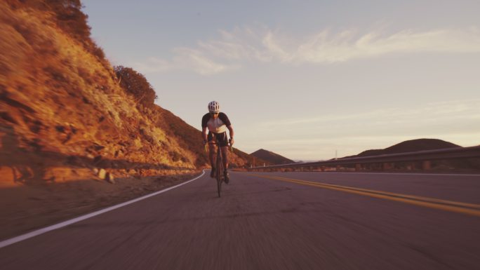 年轻健康的男子骑着公路自行车在夕阳下山