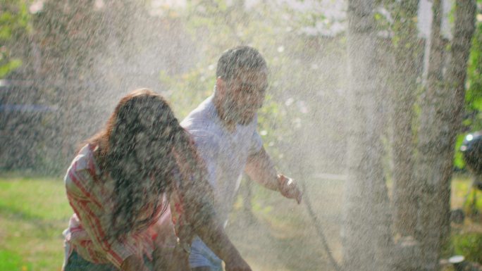 一对快乐的年轻夫妇在炎热的夏天玩着花园里的喷水器