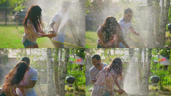 一对快乐的年轻夫妇在炎热的夏天玩着花园里的喷水器