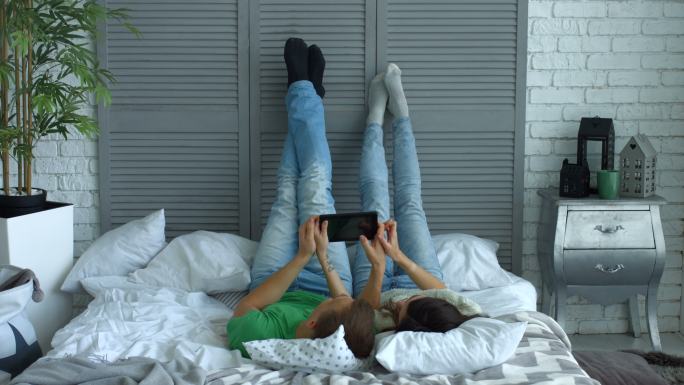 情侣在躺在床上玩着平板电脑