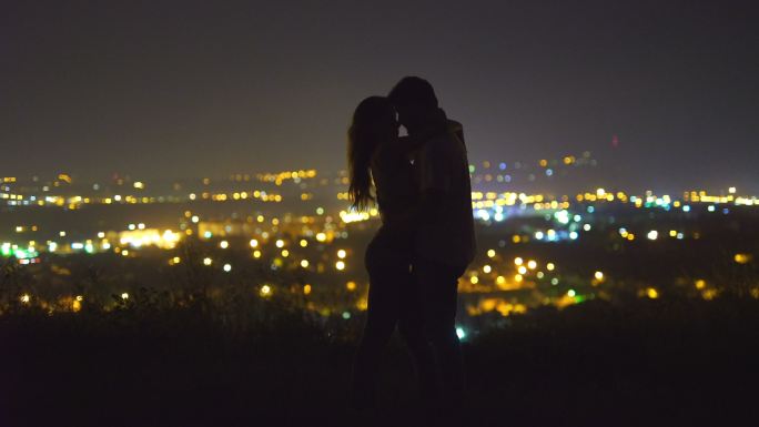 这对情侣在城市灯光的背景下接吻。