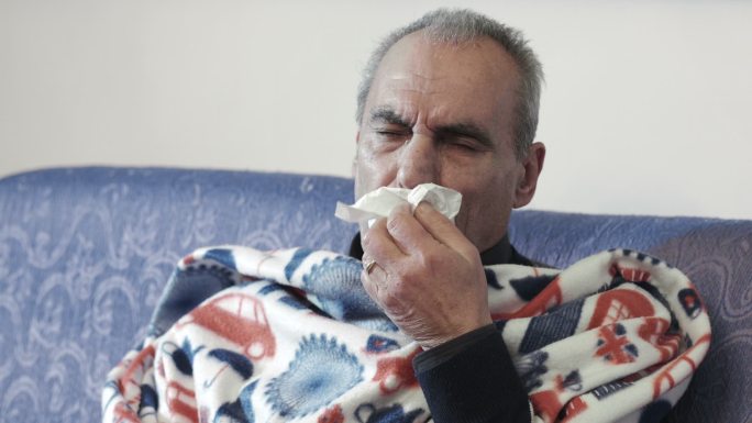 发烧感冒的生病老人：盖着毯子坐在沙发上