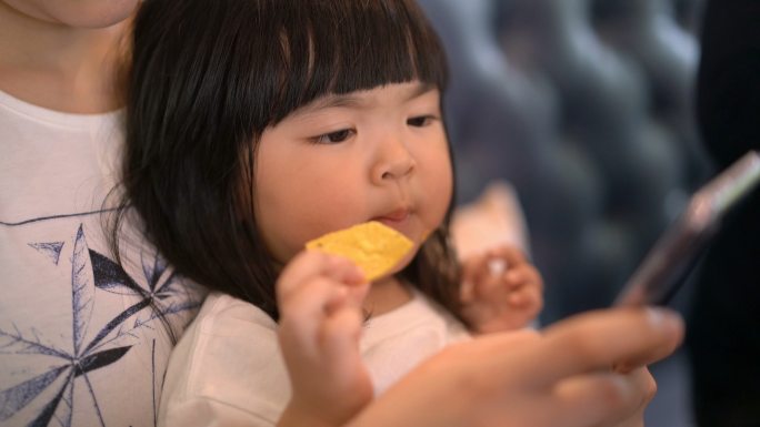 幼儿吃薯片，妈妈用智能手机和自拍