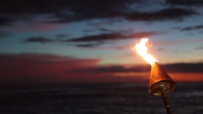 日落时分热带海滩上的提基火炬火焰