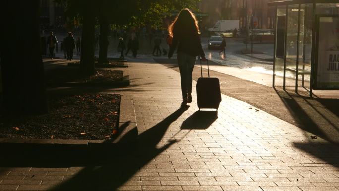女孩拉着行李箱沿着空荡荡的人行道走远