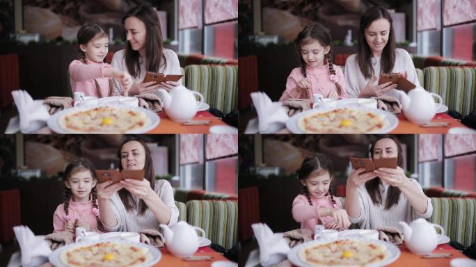 妈妈和女儿在比萨店用手机拍比萨