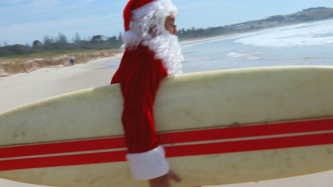 圣诞老人拿着冲浪板在海滩上跑步