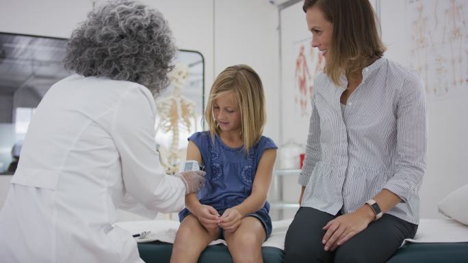 小学生坐在检查台上，医生检查她的血压