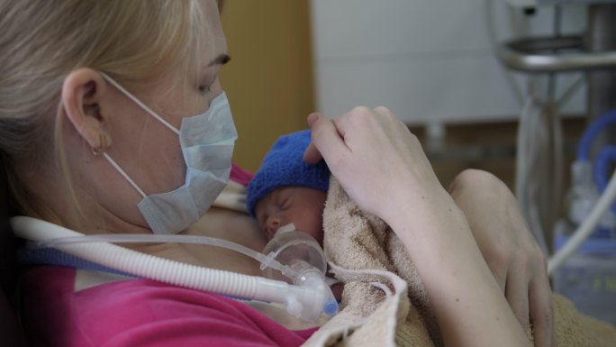 一位戴着医用口罩的妇女抱着一个新生婴儿