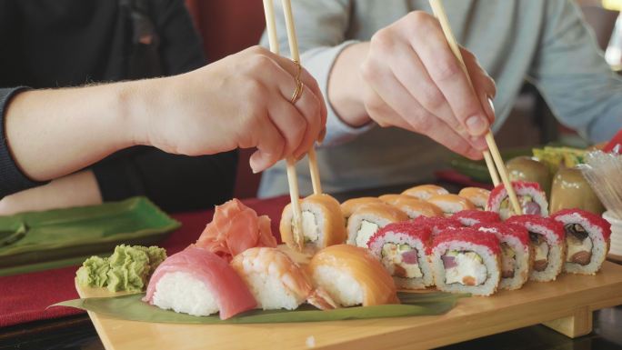 年轻夫妇拿着筷子从盘子里拿寿司。