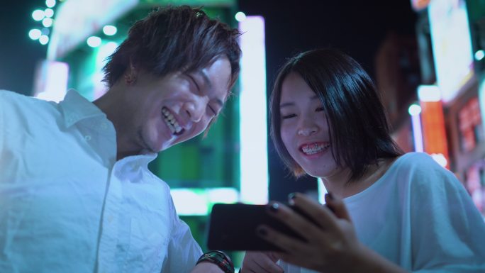 年轻的夫妇交谈，大笑，使用手机共享屏幕。