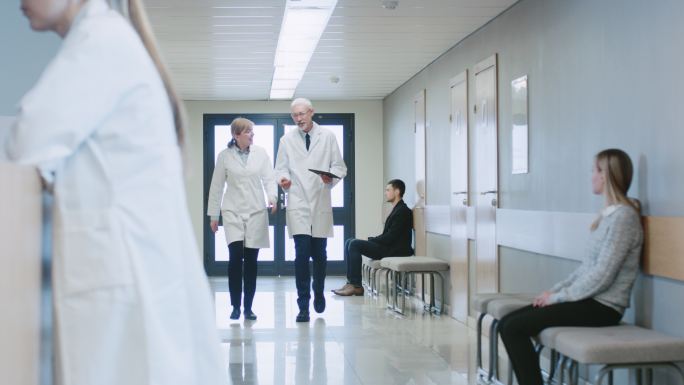 两位医生穿过医院的走廊手持平板电脑并交谈