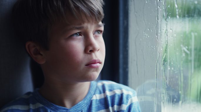 一个悲伤的小男孩在家透过窗户看雨