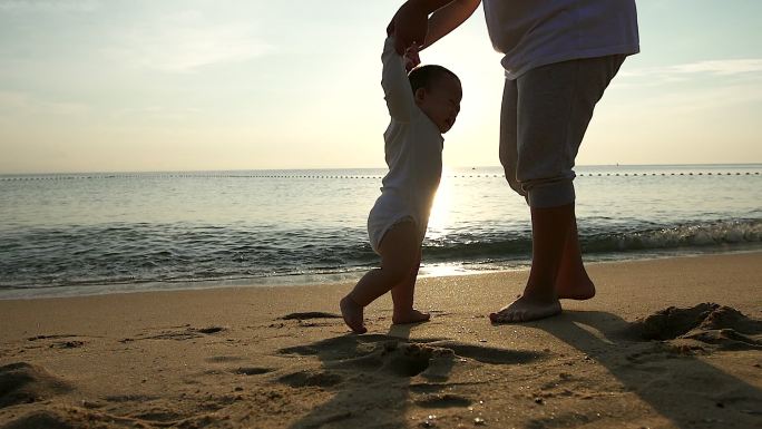 母亲帮助婴儿学习走路在沙滩上。