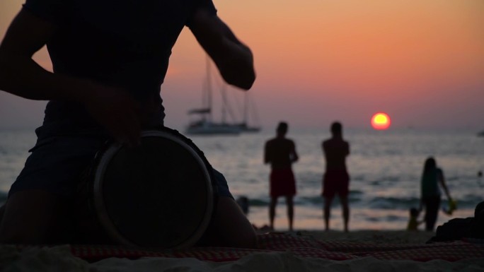 日落时分，一个男人在海滩上玩德杰姆贝鼓