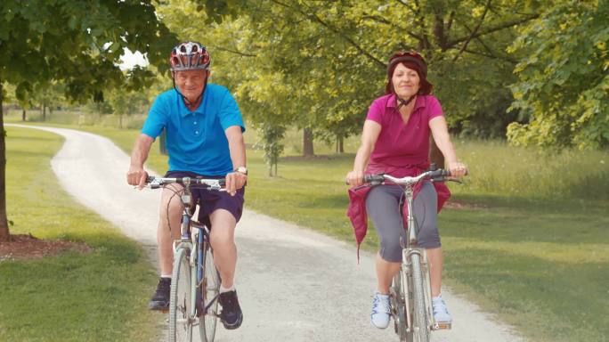 一对老年夫妇骑着自行车穿过公园