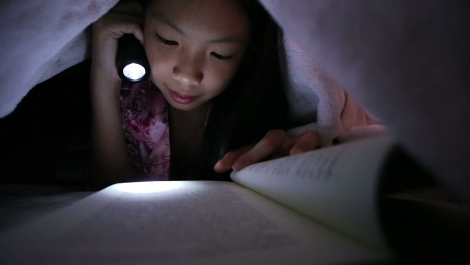 小女孩在床上用手电筒看书