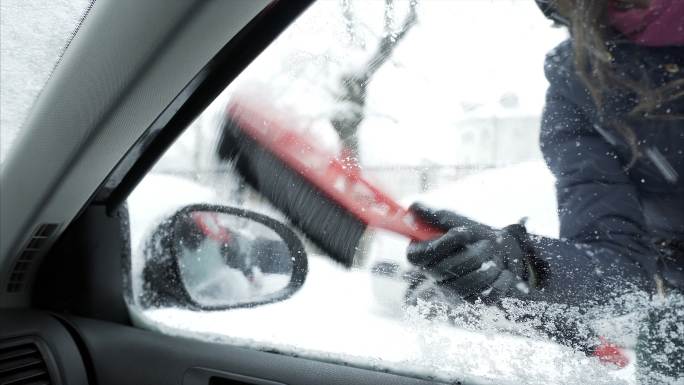 清除车窗和后视镜上积雪的年轻女子。