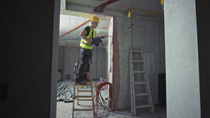 建筑工人站在梯子上使用电钻